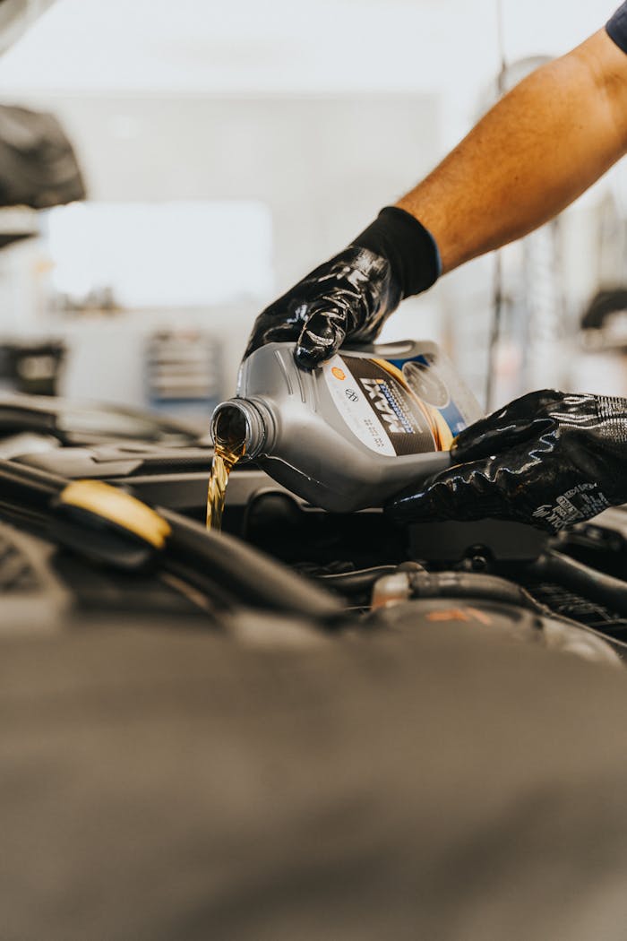 services-03 Close-up of a mechanic pouring engine oil into a car engine with gloved hands, indoors.