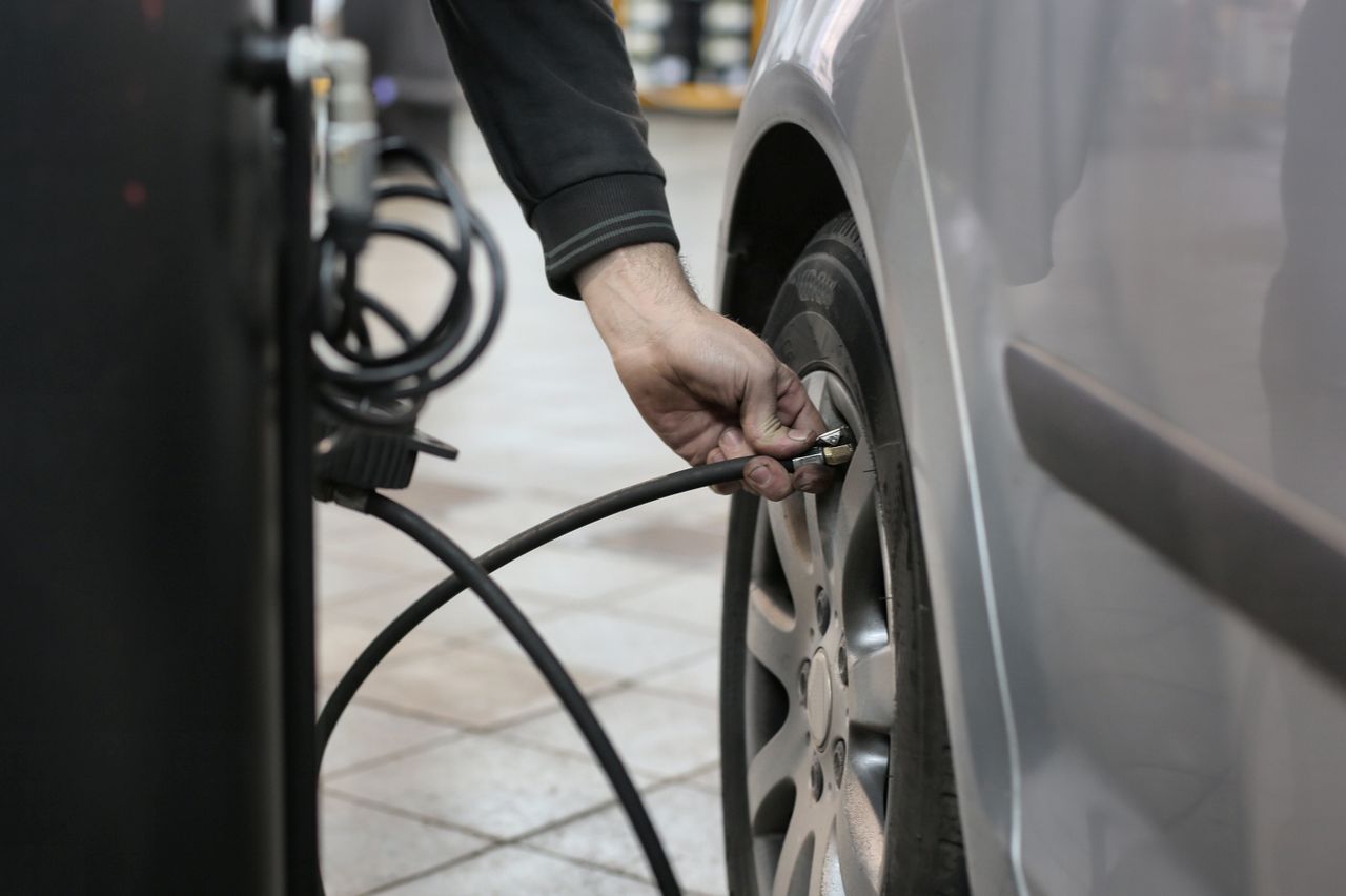 why-choose-us Mechanic inflating a car tire inside an auto repair shop, ensuring optimal tire pressure.