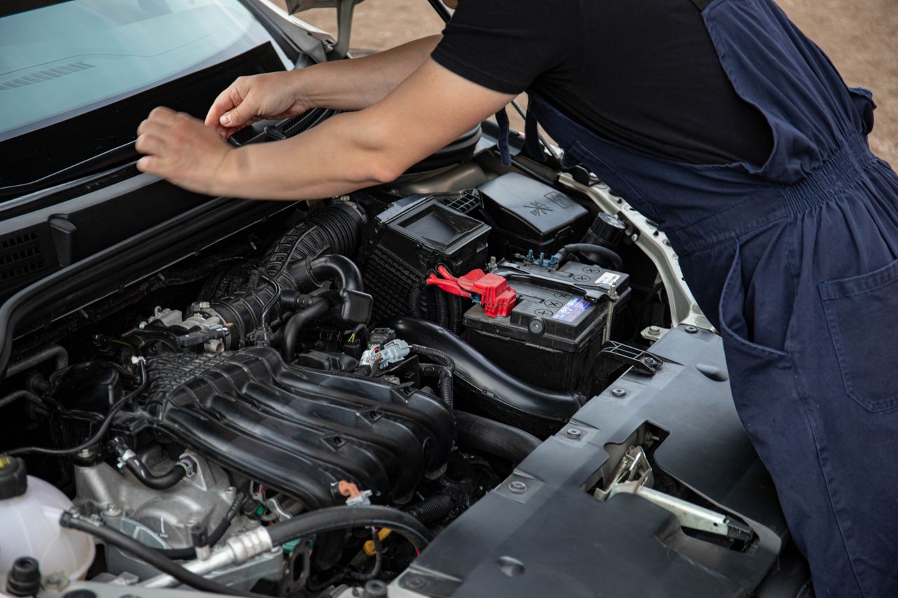 hero-img-01 Mechanic performing maintenance on a car engine outdoors during the day.