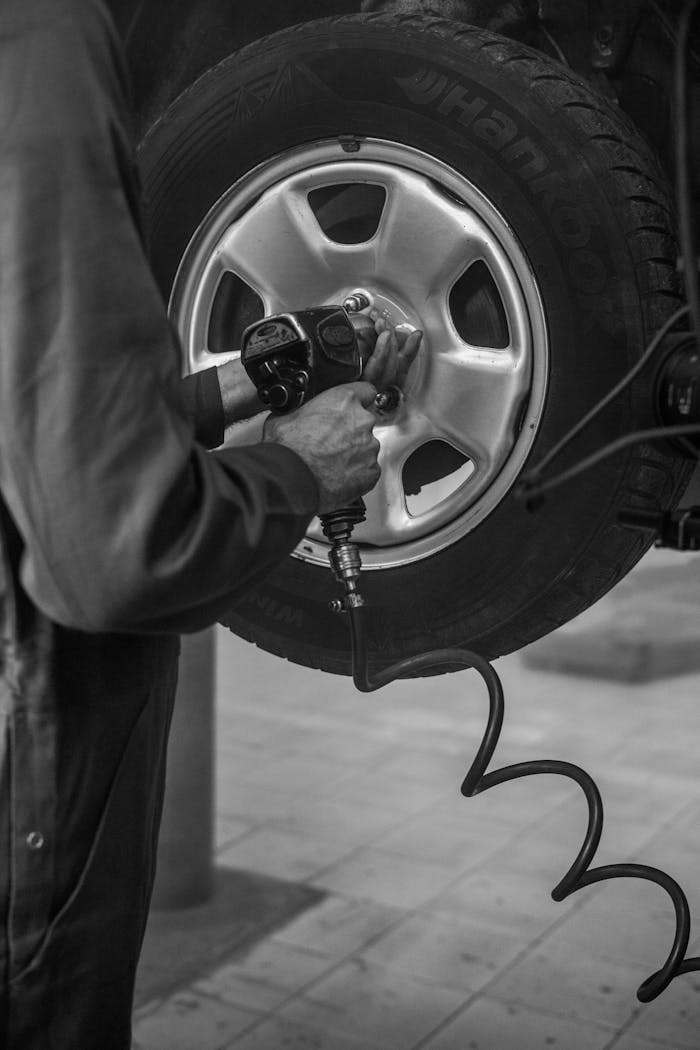 hero-img-02 Mechanic uses air wrench to fix car tire in a monochrome garage setting.
